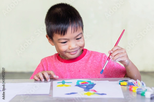 Fototapeta Portrait image of 5-6 yeas old child boy. Asian student drawing and painting colours on the paper in the room. Study​ from​ home, social​ Distance, Kid and education concept.