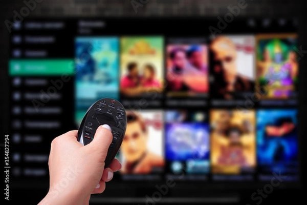 Obraz Multimedia streaming concept. Hand holding remote control. TV screen with lot of pictures.