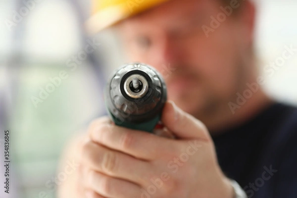 Obraz Arms of worker using electric drill closeup