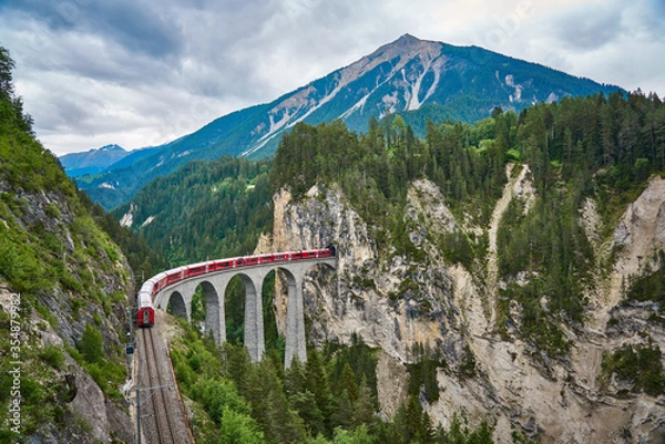 Fototapeta Red train passes above the Landwasser Viaduct bridge, in canton of Graubünden, Switzerland. Bernina Express / Glacier Express uses this railroad.