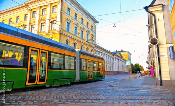 Fototapeta helsinki street with green yellow public tram and big square with old buildings  in background, Finland