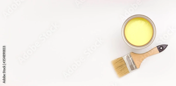 Fototapeta A paintbrush and a can of yellow paint on the side on a light background. Top view, banner. Renovation concept.