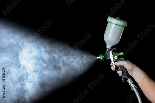 Obraz a hand in a rubber glove holds a mechanical atomizer. Holds the trigger, he sprays. Black background