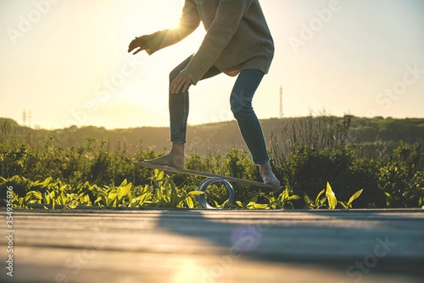 Fototapeta side view of healthy beautiful active woman keeping balance on the wooden balance board against the sky background at sunset summer day. Activity and outdoor concept.