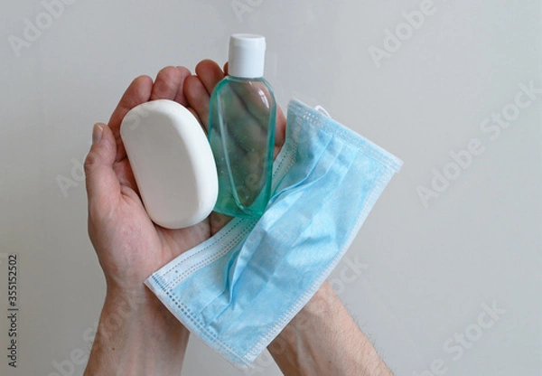 Fototapeta Man holding surgical mask, hand sanitizer and a soap, man's hands full of coronavirus prevention consumables isolated on white background