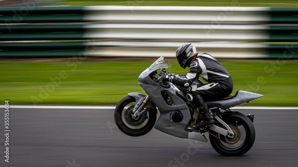 Fototapeta A panning shot of a grey racing bike on one wheel as it circuits a track