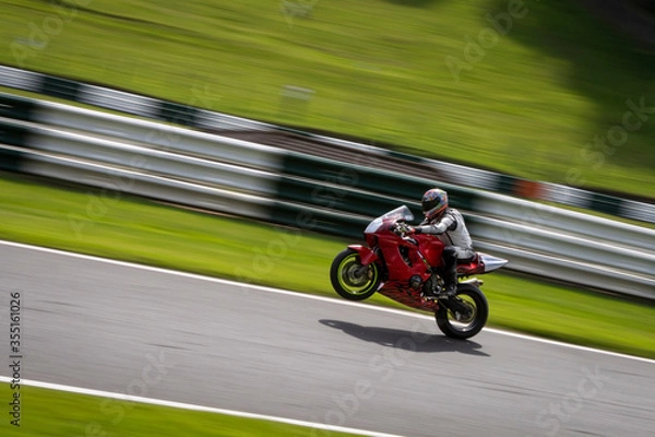Fototapeta A panning shot of a red racing bike on one wheel as it circuits a track