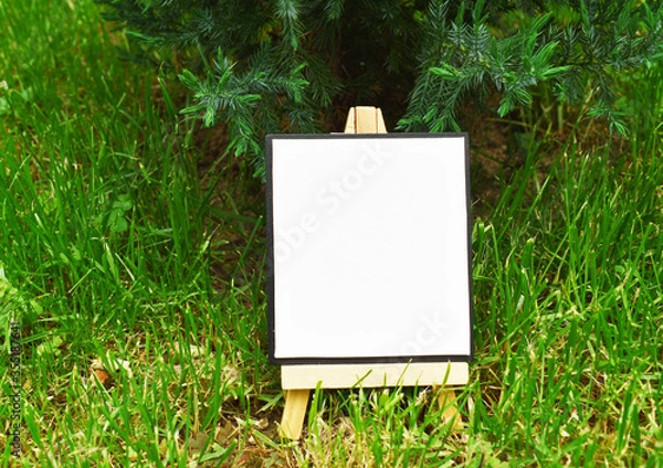 Fototapeta Mock up blank canvas on wooden easel in a green ivy garden, empty poster, banner, board