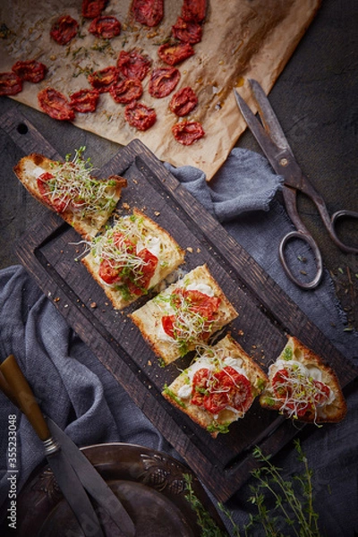 Obraz Italian bruschetta with homemade sun-dried tomatoes and  stracciatella cheese on grilled crusty bread, fresh baguette with burrata cheese and sun-dried tomatoes on cutting wooden board, top view 