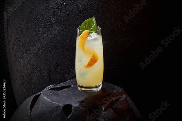 Obraz Glass of lemonade with a fresh Basil leaf, orange zest and ice cubes on a dark stone background, copy space, empty space 
