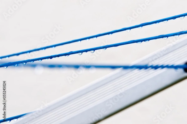 Fototapeta Blue clothing lines of a clothes spin with many raindrops at the string in front of a light background, after the rain. Retro way of doing the laundry.