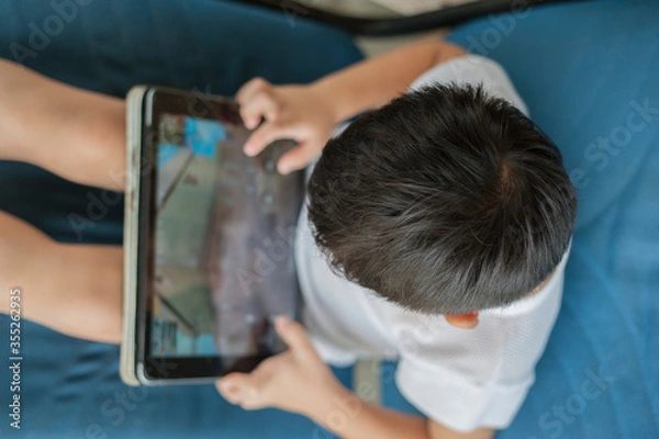 Fototapeta Penang, Malaysia - January 14, 2020 : Little kid's using digital touchscreen phone tablet computer playing games.
