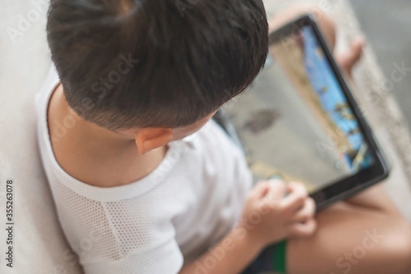 Fototapeta Penang, Malaysia - January 14, 2020 : Little kid's using digital touchscreen phone tablet computer playing games.