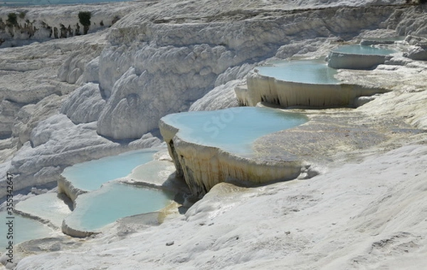 Fototapeta Pamukkale, Turkey. This region is a touristic city famous for its travertine formed by leaving white residue on the rock structure due to the water coming out of the rich carbonated water source.