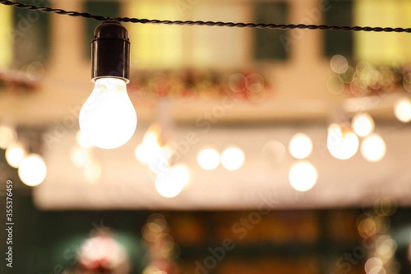 Obraz Glowing bulb on wire against blurred lights. Space for text