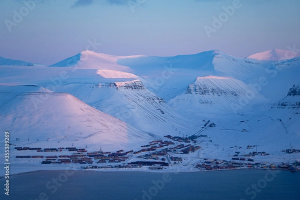 Fototapeta View over Longyearbyen and the snow covered mountains with pink light in March