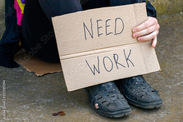 Obraz unemployed in old shoes holds in his hand a cardboard tablet with the inscription need work on the ground are small coins of alms.