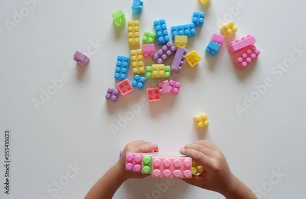 Fototapeta Close up of child's hands playing with colorful plastic bricks at the table. Toddler having fun and building out of bright constructor bricks. Early learning. stripe background. Developing toys
