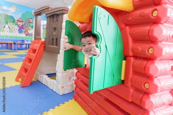 Obraz An Asian boy wearing a white shirt is playing a toy house in the playground.