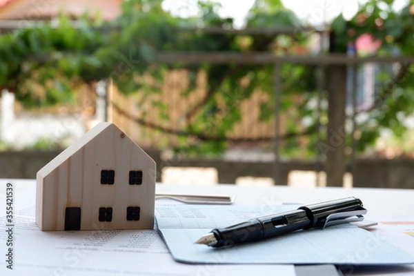 Obraz Model of house and pen placed on a bank book on table on blurred background