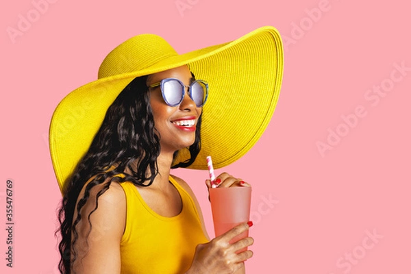 Obraz Profile portrait of a young smiling woman with yellow summer hat and sunglasses holding a drinking cup and paper straw