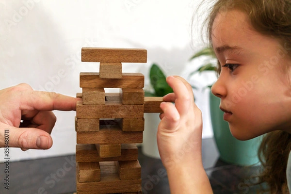 Obraz Father and daughter playing game Tumble tower from wooden block together