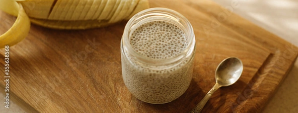 Fototapeta Dessert bowl of tasty chia seed pudding and banana on wooden table on white background. Banner for website