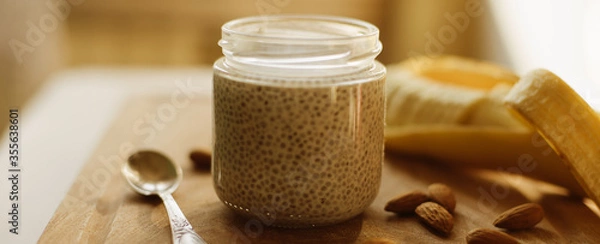 Fototapeta Dessert bowl of tasty chia seed pudding and banana, almond on wooden table on white background. Banner for website