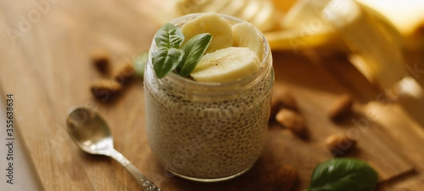 Fototapeta Vegan Chia Pudding with Banana and almond on wooden background. Vegan, morning, breakfast, healthy eating concept. Banner for website