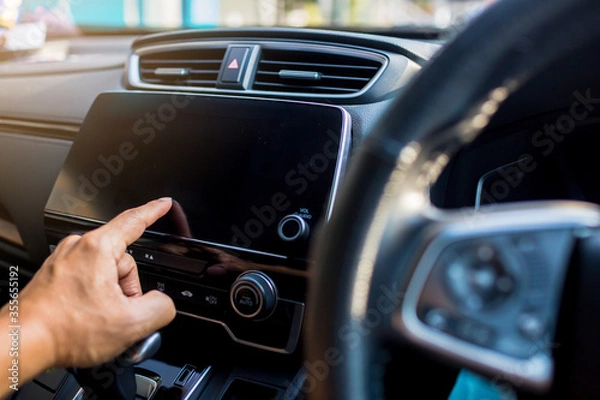 Fototapeta Selective focus to driver's finger touch on the smart monitor screen at the console in the car. The concept of smart car.