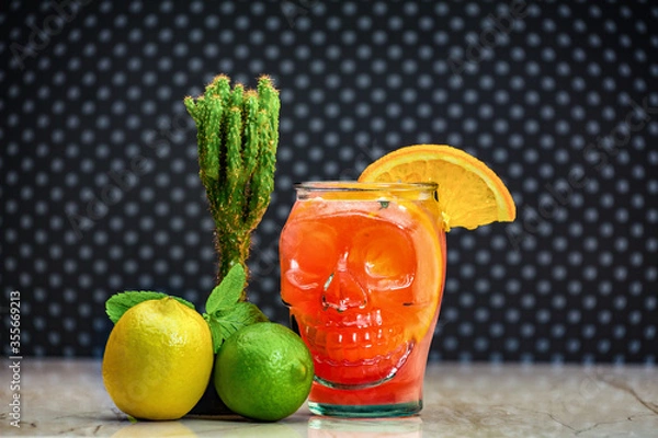 Obraz Fresh juice, alcohol, ice and an unusual mug in the shape of a head. Alcoholic halloween zombie cocktail consisting of absinthe, ru, cranberry and grapefruit juice in a glass skull-shaped.