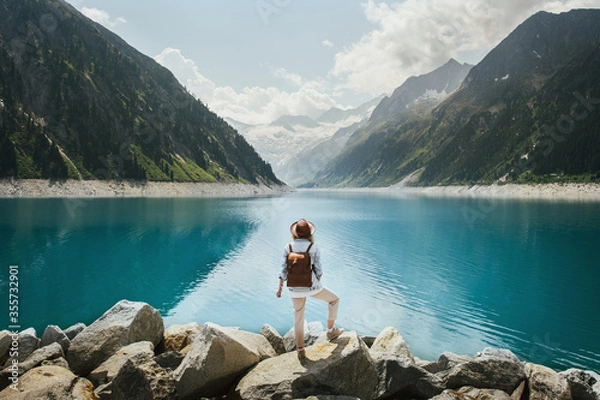 Fototapeta Travelers girl look at the mountain lake. People with a backpack travel. Adventure and travel in the mountains region. Zillertal Alps, Austria.