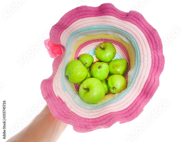 Fototapeta Green apples in a colorful straw hat towards white held in one hand