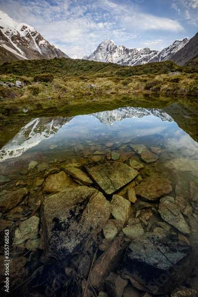 Fototapeta High alpine lake reflection of mountain with rocks in the foreground