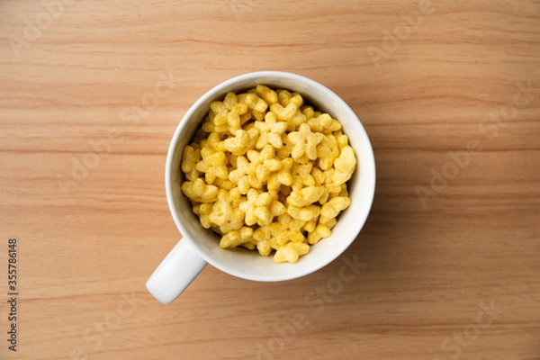 Obraz Star shaped honey coated cereal in a white glass and wooden background.