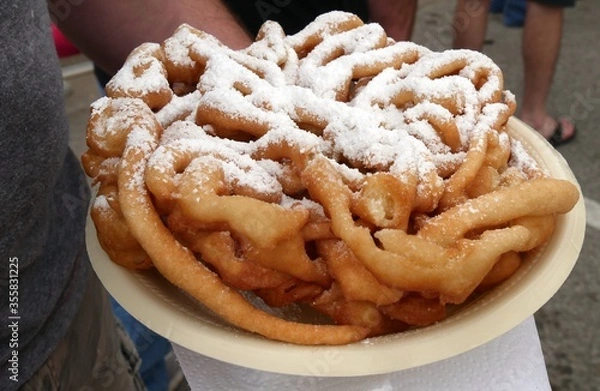 Fototapeta A hand holding a plate of funnel cake with powdered sugar on top
