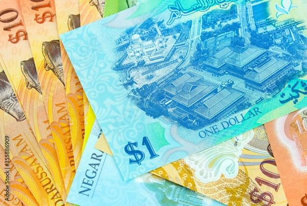 Fototapeta Close-up of colourful brunei dollar banknotes in various value $1, $5, $10, $100 over white. Focus on banknotes.
