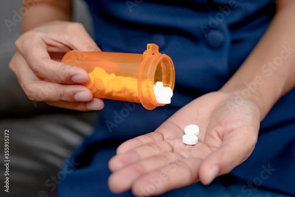 Obraz Close up of working woman taking in pill she is pours the pills out of the bottle,taking painkiller to reduce sharp ache concept,health care and medicine concept.