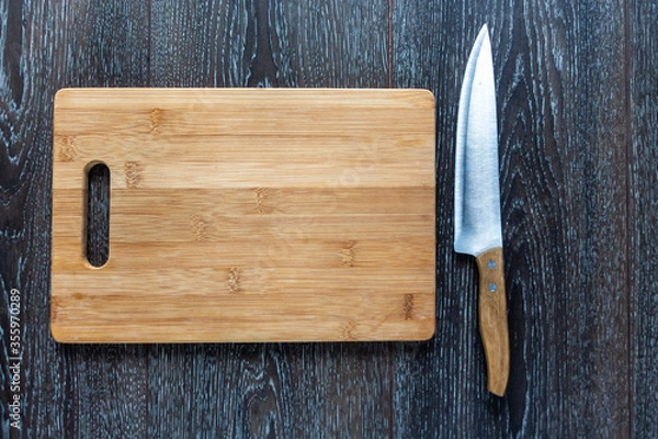 Obraz Wooden cutting board and a knife liyng on a dark background. Top view. Copy space for text