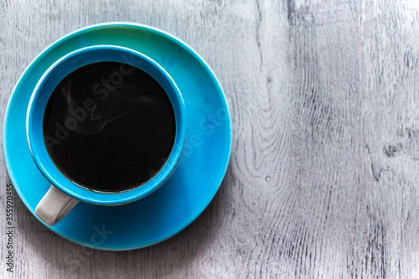 Obraz Blue cup of hot coffee on a saucer stands on a gray wooden background, top view. Copy space for text.