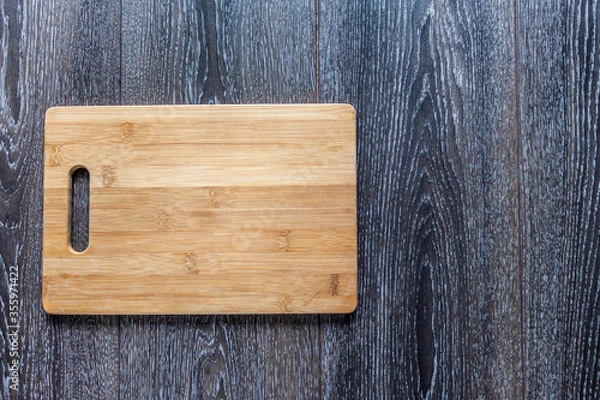 Obraz Wooden cutting board liyng on a dark wooden background. Top view