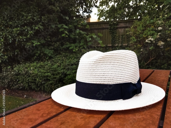 Obraz White hat with black detail on a wooden table in the garden