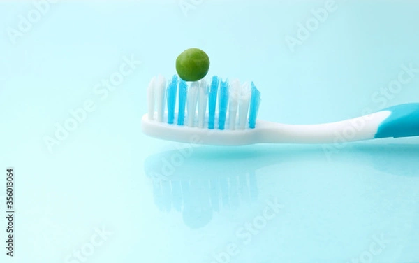 Fototapeta A tooth brush on a hygienic background, with a green pea on it.  People should use the size of a pea amount fluoride toothpaste on brush concept. Could be used for dental care education.