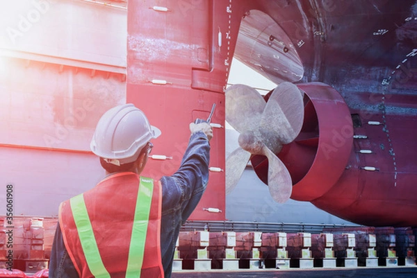Obraz Shipyard ship repair worker with Talkie hand holding for shafting port controller, surveyor, inspecting the final repairing of propeller on dry dock. Detail of Propeller at dry dock in shipyard.