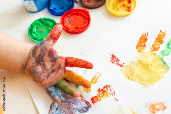 Fototapeta Close up of colored hand print on white background. Ideas for drawing with finger paints. Finger painting for kids. Little girl painting by finger hand paint color. Children development concept.