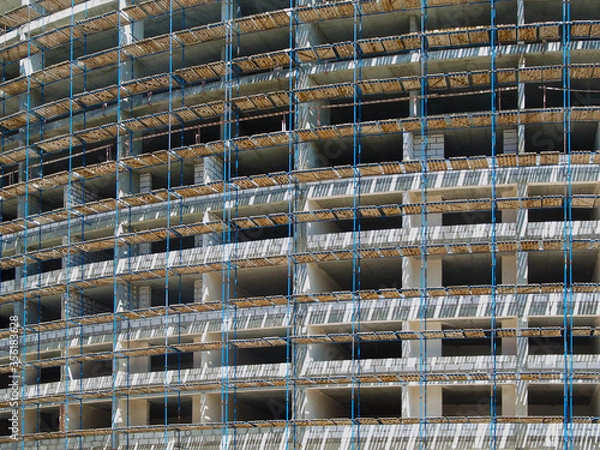 Fototapeta A lot of scaffolding on the facade of a building under construction. Construction of a monolithic house.
