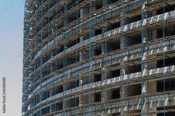 Fototapeta A lot of scaffolding on the facade of a building under construction. Construction of a monolithic house.