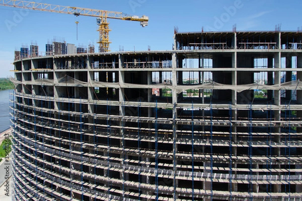 Fototapeta Yellow tower crane. Skeleton of a monolithic multi-storey building; with scaffolding on the facade. Great construction site.