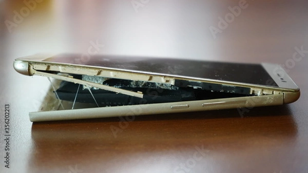 Fototapeta Swollen smartphone battery. Damaged smartphone with a faulty battery. Damaged phone on a wooden background.
