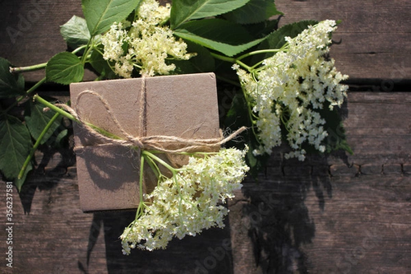 Fototapeta Brown craft gift box decorated with natural herbs and flowers on old wooden background with copy space. Floral decor elements. Father`s day gift concept.
